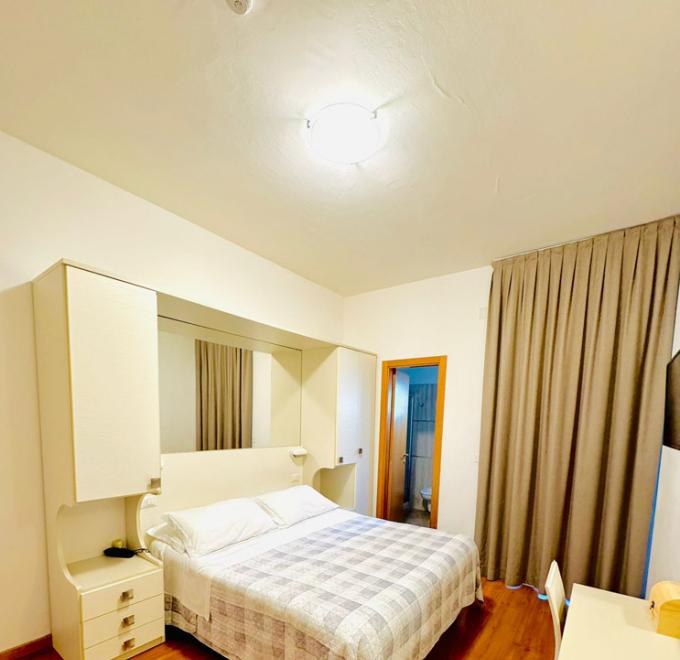 Cozy room with double bed, beige curtains, and wooden floor.