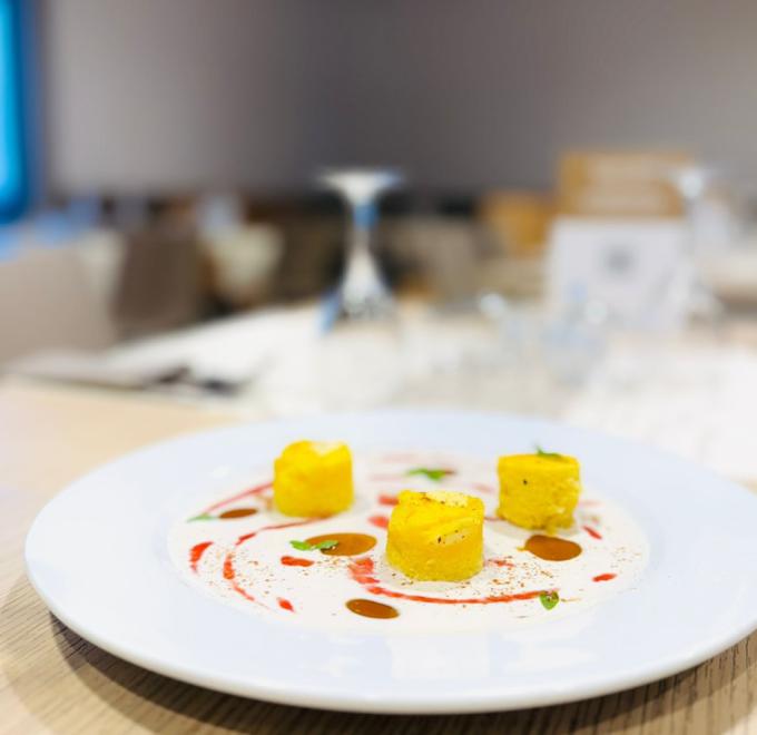 Three yellow cubes on elegant plate, creamy sauce, and colorful drops.