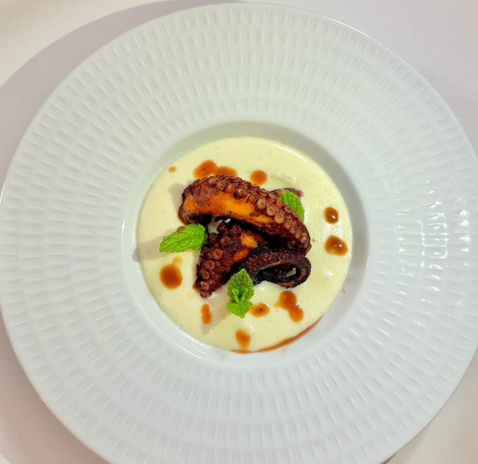 Grilled octopus on white cream, garnished with mint and brown sauce drops.